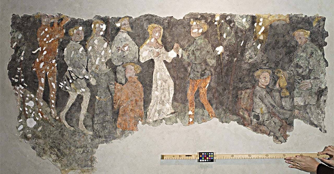 Large section of a fresco showing a group of people, around a man and woman in the center holding hands. A person is holding up a yard stick underneath the fresco. The yardstick has a small color-matching grid attached to it.