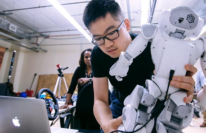 Graduate student Jin Xu sets up the NAO in the lab. A cable connects the robot to the laptop.